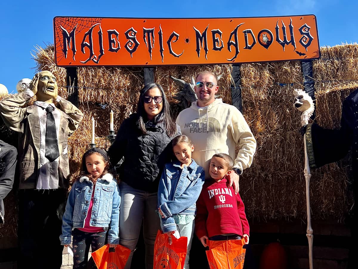 A family with trick-or-treat bags under the Majestic Meadows Halloween sign